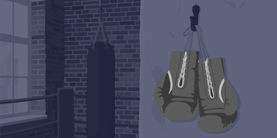 Ein Boxsaal in Dämmerlicht: An einer Backsteinwand neben einem Fenster hängt ein Boxsack, rechts hängt ein Paar Boxhandschuhe.