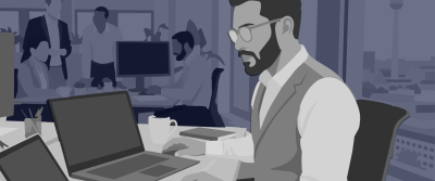 Ein bärtiger Mann mit Brille und Weste arbeitet im Großraumbüro an einem Laptop; im Hintergrund Kolleginnen und Kollegen sowie der Berliner Fernsehturm hinter dem Fenster.