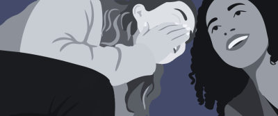 Zwei Frauen stehen eng beieinander vor blauem Hintergrund. Die linke Frau mit langen Haaren hält sich eine Hand vor den Mund und flüstert der rechten, lachenden Frau mit lockigem Haar etwas ins Ohr.