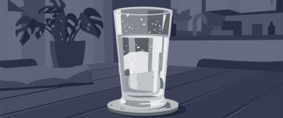 Ein bis zur Hälfte mit Wasser gefülltes Trinkglas steht auf einem Untersetzer auf einem Holztisch. Im Hintergrund eine Zimmerpflanze und eine angedeutete Küche.