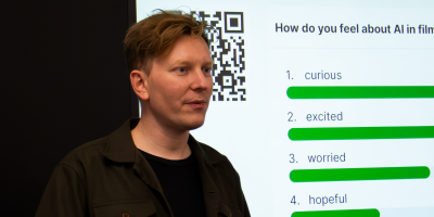 Tobias M. Huber steht im Profil vor einer Präsentationsleinwand mit einem QR-Code und einer Live-Umfrage